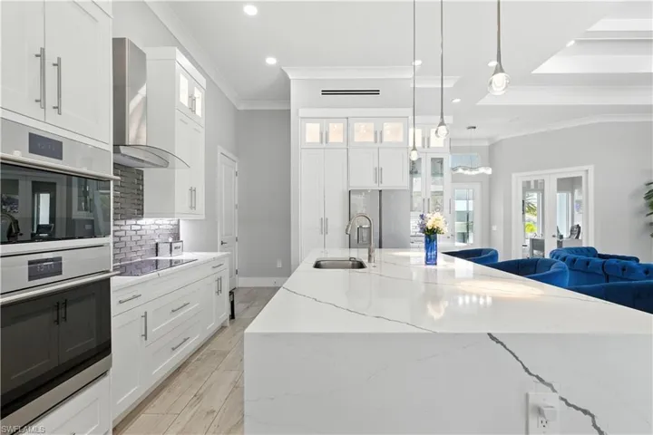 Kitchen with wall chimney range hood, crown molding, appliances with stainless steel finishes, decorative backsplash, and light stone countertops