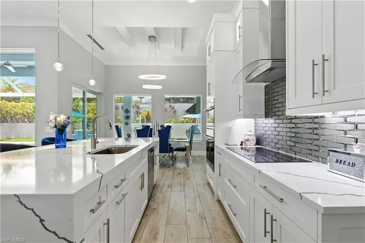 Kitchen featuring wall chimney exhaust hood, white cabinets, backsplash, light wood-style floors, and ornamental molding