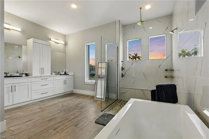 Bathroom with a soaking tub, double vanity, a marble finish shower, and wood finished floors