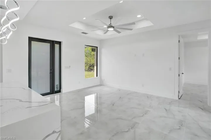 Unfurnished room with a raised ceiling, light marble finish floors, ceiling fan, and recessed lighting