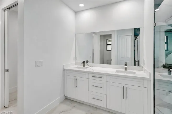 Full bath with double vanity, a marble finish shower, light marble finish flooring, and recessed lighting