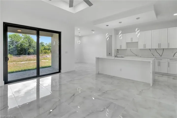 Kitchen with light stone countertops, an island with sink, white cabinetry, and light marble finish floors
