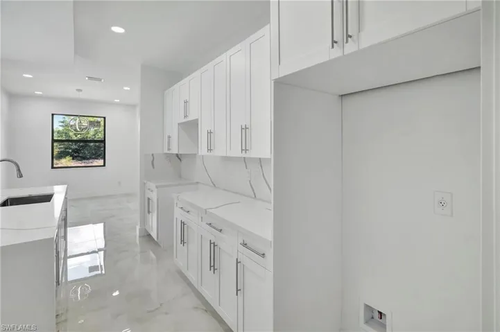 Kitchen featuring light stone counters, white cabinets, light marble finish floors, a center island with sink, and pendant lighting