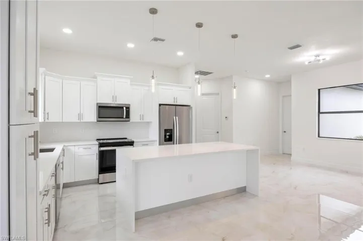 Kitchen with appliances with stainless steel finishes, light tile flooring, pendant lighting, and a kitchen island