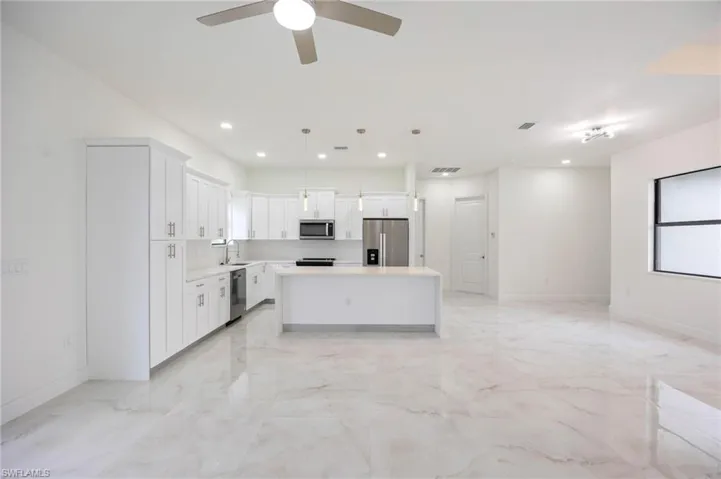 Kitchen featuring ceiling fan, decorative light fixtures, light tile flooring, a kitchen island, and appliances with stainless steel finishes
