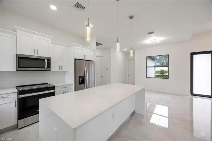 Kitchen with a center island, stainless steel appliances, light tile flooring, and white cabinetry