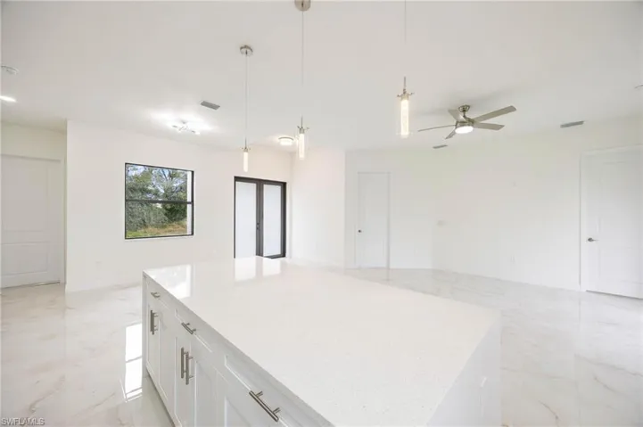 Kitchen with a center island, hanging light fixtures, white cabinets, ceiling fan, and light tile floors