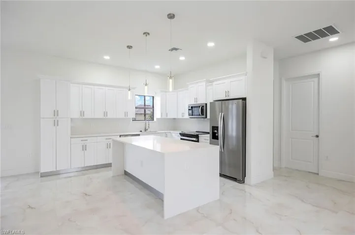 Kitchen with white cabinets, stainless steel appliances, hanging light fixtures, a center island, and sink