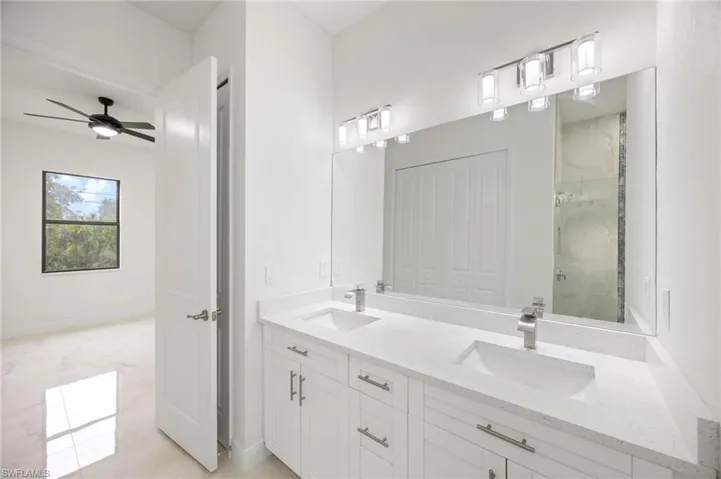 Bathroom featuring tiled shower, double vanity, ceiling fan, and tile floors