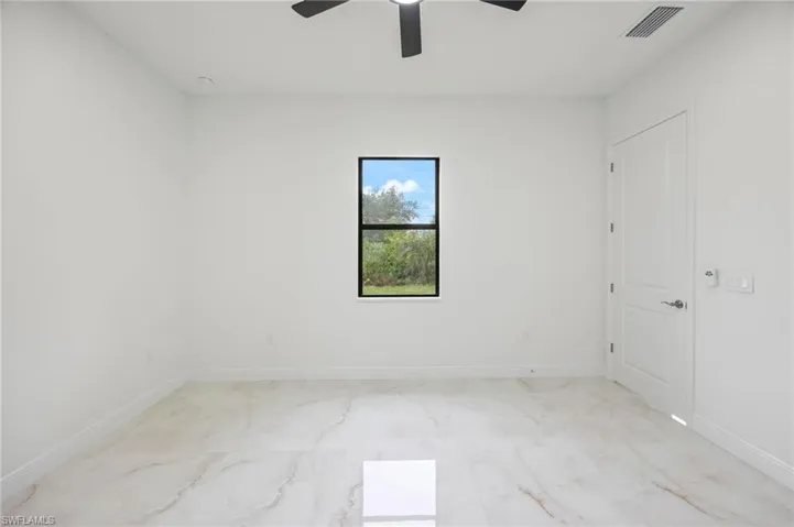 Empty room with ceiling fan and light tile flooring