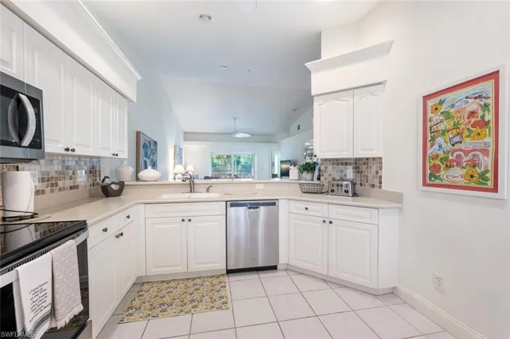 Kitchen featuring backsplash, appliances with stainless steel finishes, light countertops, light tile patterned flooring, and white cabinetry