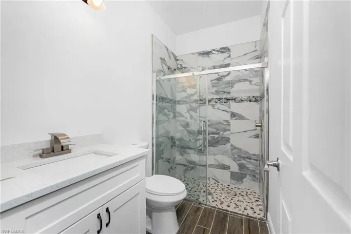 Bathroom featuring vanity, a marble finish shower, and wood tiled floors