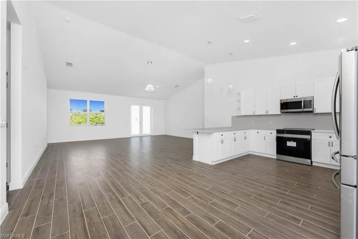 Kitchen featuring stainless steel appliances, a peninsula, light countertops, open shelves, and vaulted ceiling