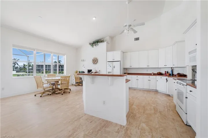 Kitchen featuring white appliances, dark countertops, high vaulted ceiling, white cabinets, and a ceiling fan