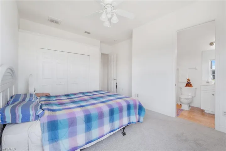 Carpeted bedroom featuring a closet, ensuite bath, and a ceiling fan