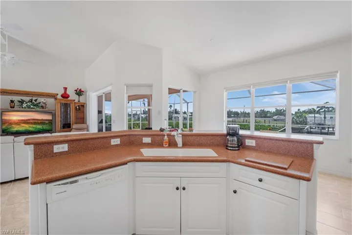Kitchen featuring white dishwasher, a sink, lofted ceiling, open floor plan, and white cabinetry