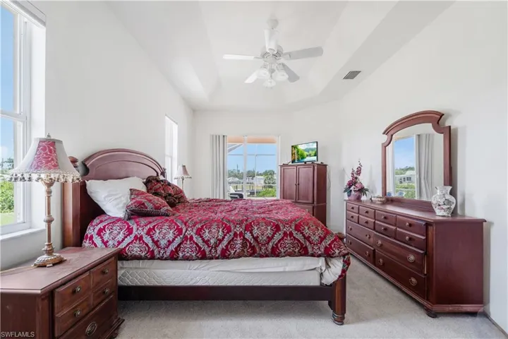 Bedroom featuring light colored carpet, a raised ceiling, and a ceiling fan