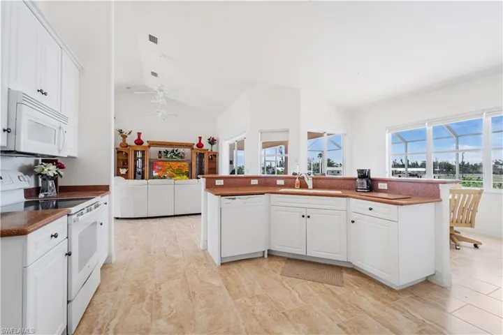Kitchen with white appliances, a sink, vaulted ceiling, white cabinetry, and a ceiling fan