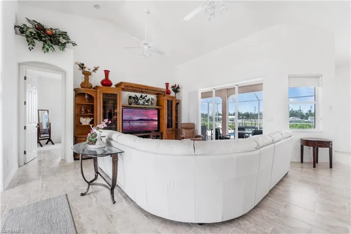 Living area with ceiling fan, arched walkways, and high vaulted ceiling