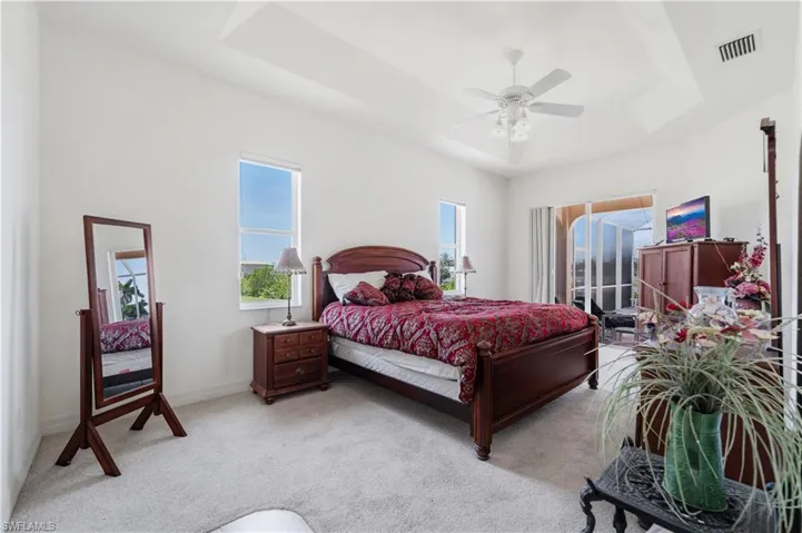 Bedroom featuring a raised ceiling, light colored carpet, ceiling fan, and baseboards