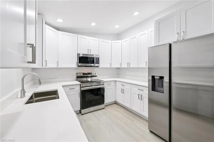 Kitchen with stainless steel appliances, white cabinetry, light wood-style flooring, light stone counters, and recessed lighting