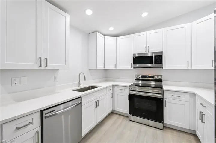 Kitchen featuring stainless steel appliances, white cabinetry, light wood-style flooring, recessed lighting, and light stone countertops
