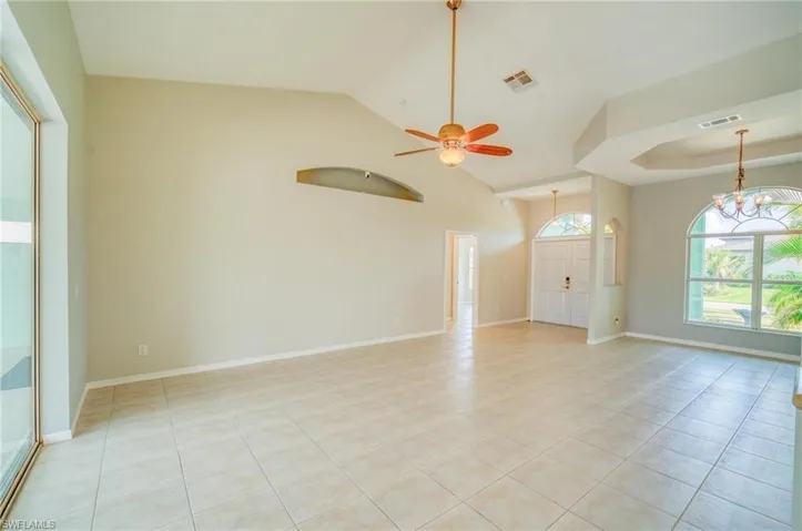 Unfurnished living room featuring light tile patterned flooring, high vaulted ceiling, a tray ceiling, and ceiling fan with notable chandelier