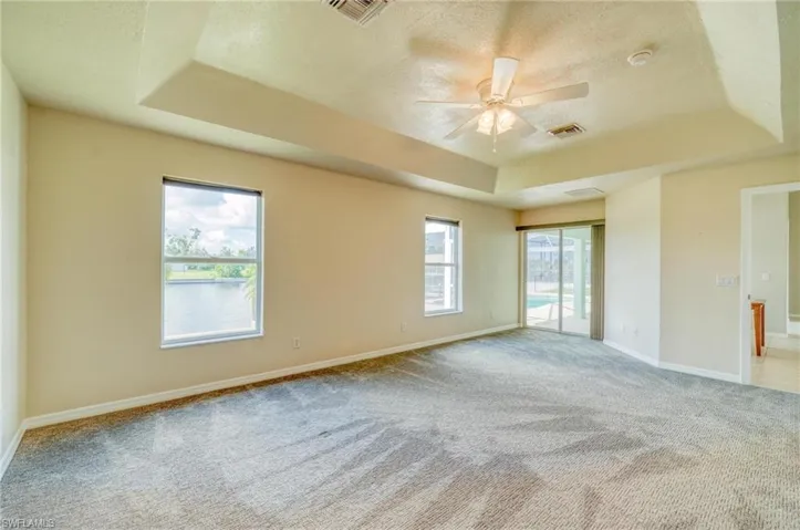 Carpeted empty room featuring a tray ceiling, plenty of natural light, and ceiling fan