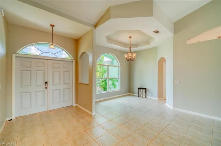 Tiled foyer featuring a tray ceiling and an inviting chandelier