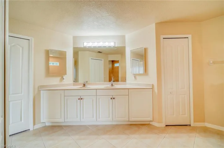 Bathroom featuring a textured ceiling, tile patterned floors, and dual vanity