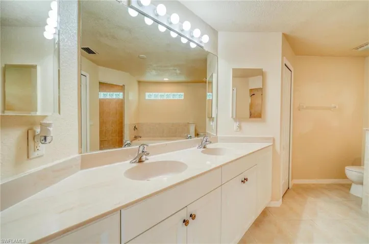 Bathroom featuring a textured ceiling, toilet, tile patterned flooring, dual vanity, and a tub to relax in