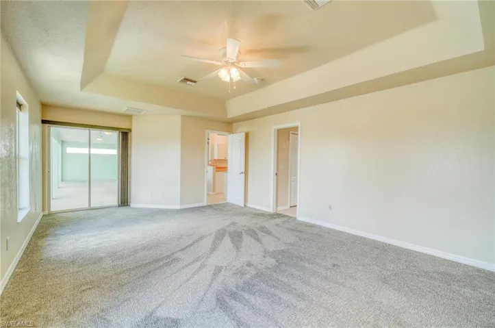 Unfurnished bedroom featuring ceiling fan, carpet flooring, and a tray ceiling