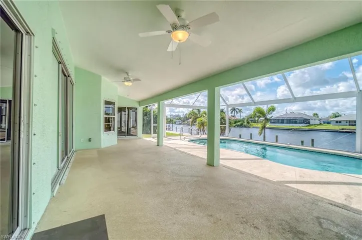 View of pool with glass enclosure, a water view, a patio area, and ceiling fan