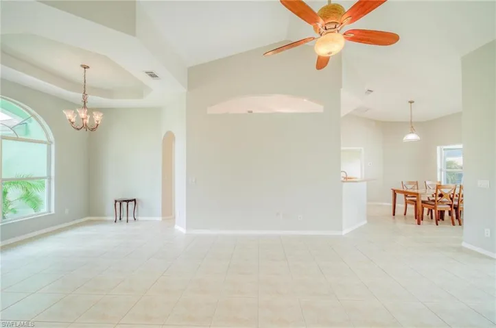 Spare room with light tile patterned flooring, a raised ceiling, and ceiling fan with notable chandelier