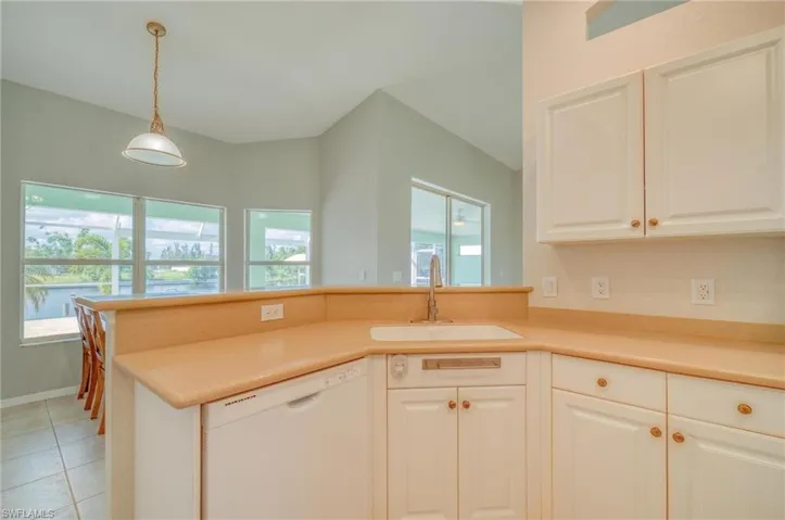 Kitchen with white dishwasher, kitchen peninsula, white cabinets, light tile patterned floors, and sink