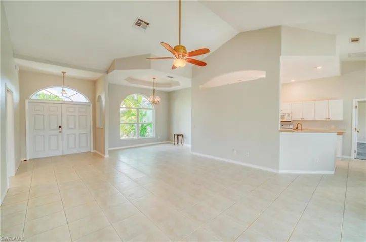 Unfurnished living room with light tile patterned floors, high vaulted ceiling, ceiling fan with notable chandelier, and a raised ceiling