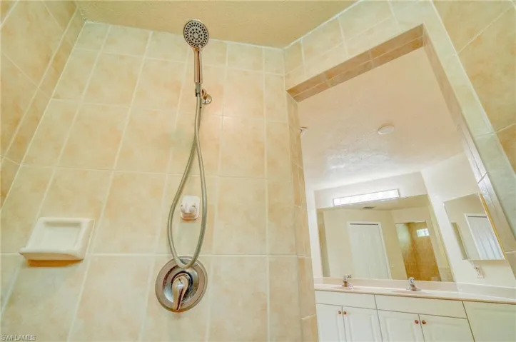 Bathroom with a textured ceiling, tiled shower, and vanity