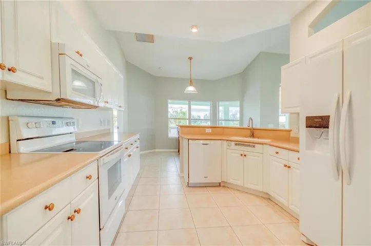 Kitchen with white appliances, hanging light fixtures, light tile patterned flooring, sink, and white cabinetry