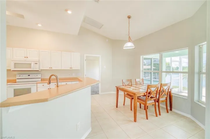 Kitchen featuring white appliances, light tile patterned flooring, pendant lighting, and white cabinetry
