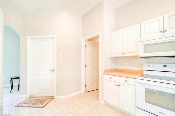 Kitchen with white cabinets, electric stove, light tile patterned floors, and a high ceiling