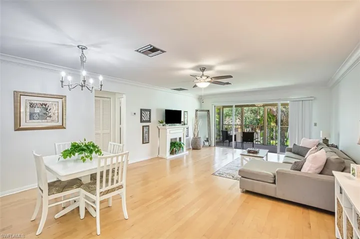 Living room with crown molding, light wood-style floors, a fireplace, ceiling fan, and a chandelier
