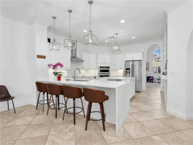 Kitchen with arched walkways, a breakfast bar, stainless steel appliances, ornamental molding, and white cabinetry