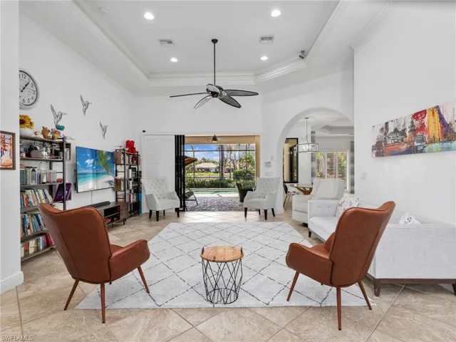 Living room with arched walkways, ornamental molding, ceiling fan, a high tray ceiling, and hanging lights