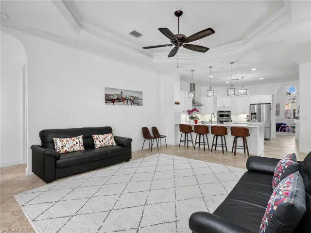 Living room with arched walkways, ornamental molding, ceiling fan, light tile patterned floors, and a raised ceiling