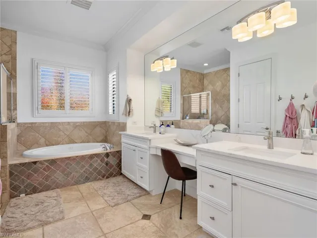 Bathroom with two vanities, a garden tub, a tile shower, and ornamental molding