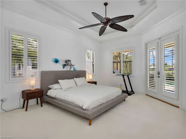 Carpeted bedroom featuring access to outside, french doors, a ceiling fan, ornamental molding, and a tray ceiling