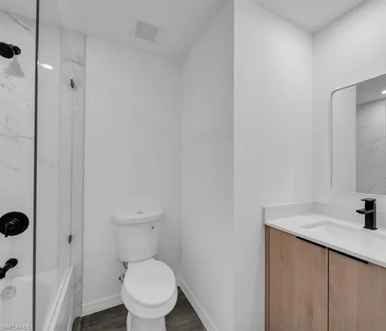 Bathroom with vanity, a combined bath / shower with marble appearance, and dark wood-style flooring