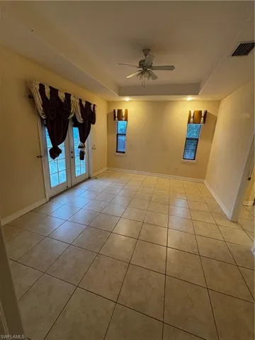 Unfurnished room featuring a raised ceiling, a ceiling fan, light tile patterned flooring, and french doors