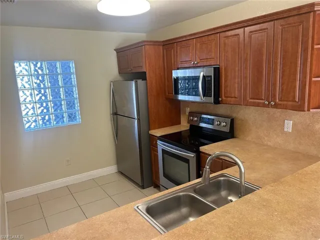 Kitchen featuring stainless steel appliances, light countertops, wood finish cabinets, and light tile patterned flooring