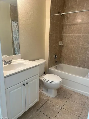 Full bathroom with a textured wall, vanity, light tile patterned floors, and shower / tub combo with curtain